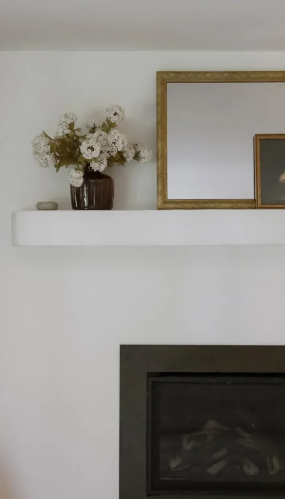 The Curated Coastal Home, North Carolina: Minimal white fireplace mantel with gilded mirror and florals